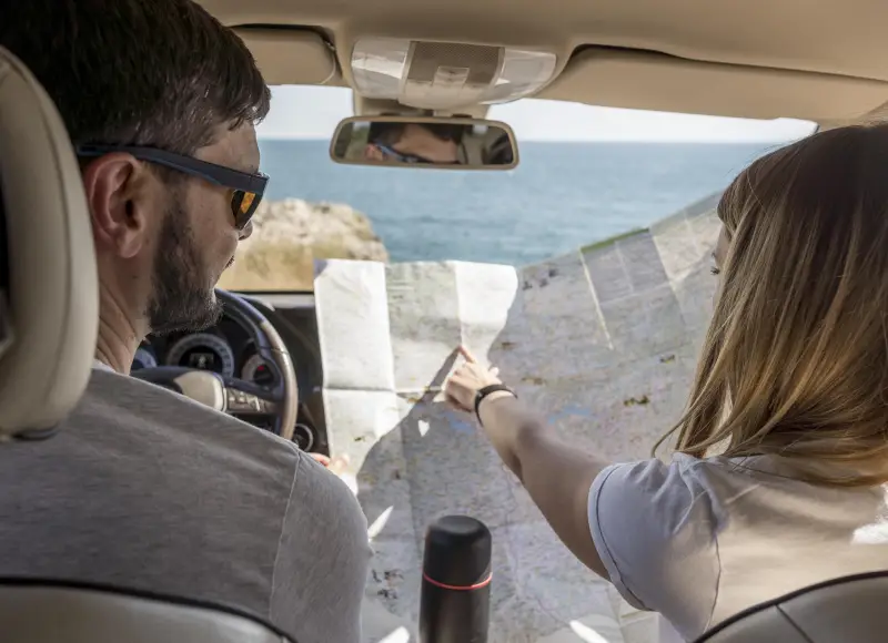 Couple looking at a map in a car overlooking the sea