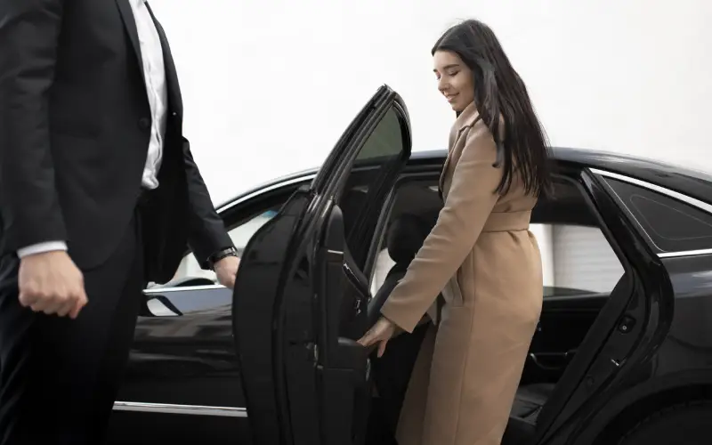 Driver holding the car door to let a young woman in.