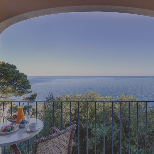 Terrace of one of the hotel rooms equipped with tables and chairs overlooking the sea.