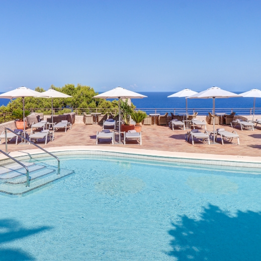 Panoramabild des Swimmingpools des Hotels mit Sonnenliegen und Sonnenschirmen und dem Meer am Horizont.