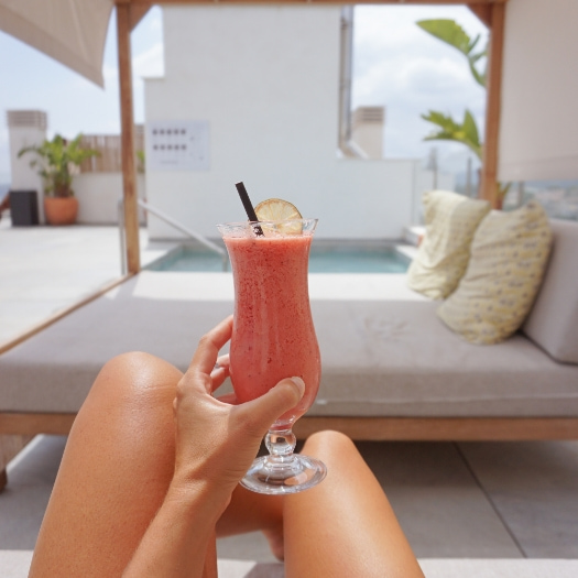 Eine Person mit einem Cocktail in der Hand liegt auf einem balinesischen Bett