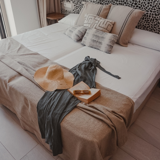 Hotelzimmer mit einem Doppelbett und einem Kleid, Pamela, Buch und Sonnenbrille auf dem Bett